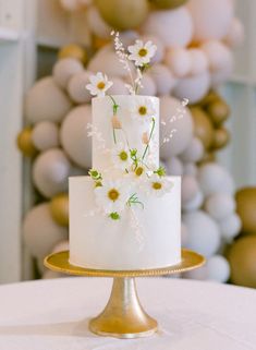 a white wedding cake with daisies and greenery on top sits on a gold plate