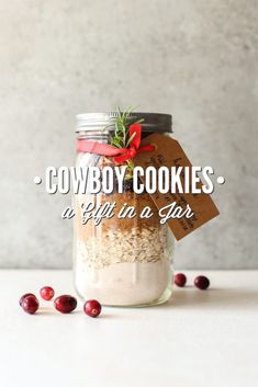 cowboy cookies in a jar with gift tags and cranberries on the table next to it