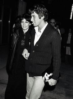 a black and white photo of a man and woman walking down the street at night