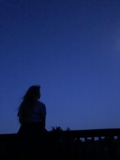 a woman standing on a bridge at night with the moon in the sky behind her