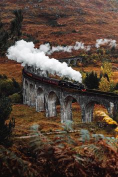 a train traveling over a bridge with steam pouring out of it