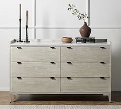 a white dresser with candles on top and a vase sitting on it's side