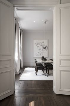 an open door leading to a dining room with white walls and wood flooring, along with a painting on the wall