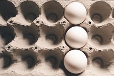 three white eggs in an egg tray on the side of a brick wall with holes