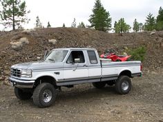 a pickup truck parked on the side of a dirt road next to a pile of rocks