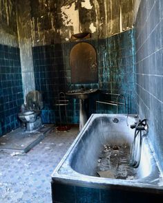 an old bathtub and sink in a run down bathroom with blue tiles on the walls