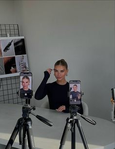 a woman holding up two cell phones in front of a camera on a tripod