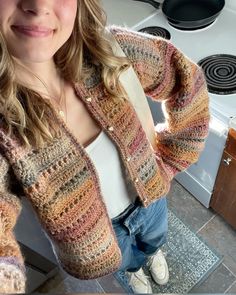 a woman standing in front of a stove top oven wearing a colorful knitted sweater