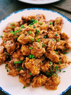 a white plate topped with meat covered in sauce and scallions on top of a wooden table