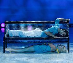 a man and woman laying on a bench in the middle of a stage show together