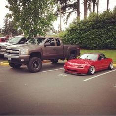 two trucks parked in a parking lot next to each other with trees and bushes behind them