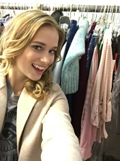 a woman standing in front of a rack of clothes and smiling at the camera with her arms crossed