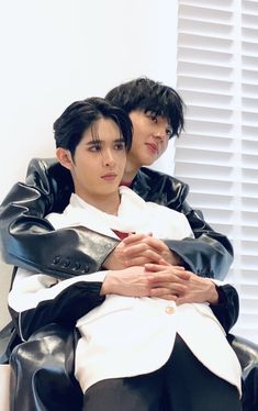 two young men sitting next to each other wearing black and white clothes, one with his arms around the other's chest