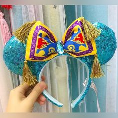 a hand holding up a mickey mouse ears headband with blue and yellow sequins