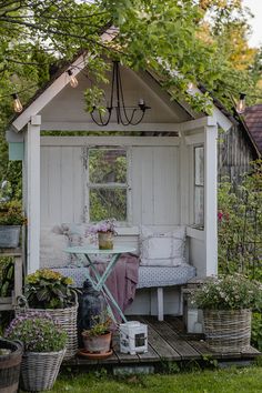 a small garden shed with potted plants and flowers in the front yard, next to a bench