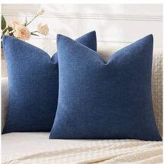 two blue pillows sitting on top of a bed next to a vase with white flowers