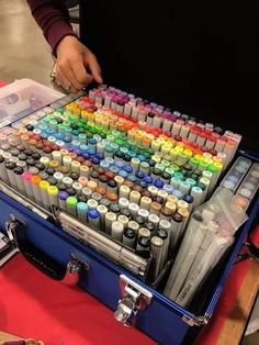 a person is holding an open case with many different colored bottles in it on top of a table