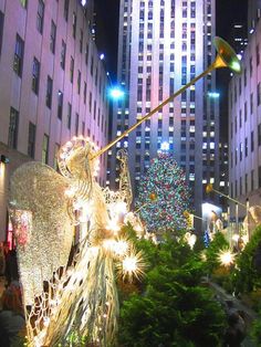 a christmas tree in the middle of a city with lights on it and an angel statue