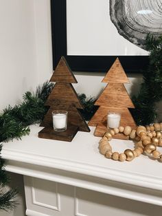 two wooden christmas trees sitting on top of a mantle next to a candle and wreath