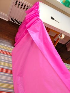 a pink cover sitting on top of a wooden floor next to a white table and chair