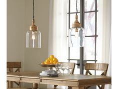 a dining room table with fruit on it and two hanging lights above the table, in front of a window