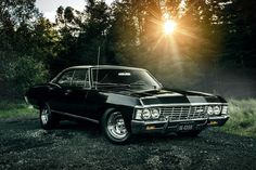 an old black car parked on the side of a road in front of some trees