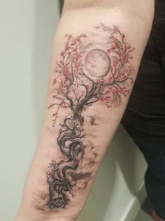 a woman's arm with a tree and moon tattoo on the left side of her arm