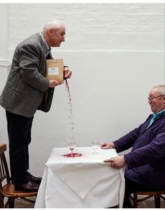 two men sitting at a table and one is pouring wine