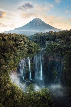 an aerial view of a waterfall in the middle of trees and mountains, with mist rising from the top