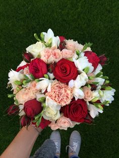 a bridal bouquet with roses and tulips is held by someone's feet