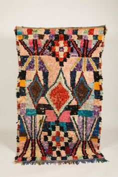 a multicolored rug with fringes and designs on the front, sitting on a white surface