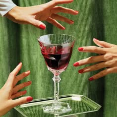 three hands reaching for a glass of wine on a clear serving tray with green cloth