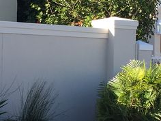 a cat sitting on top of a white fence next to bushes and trees in front of a house