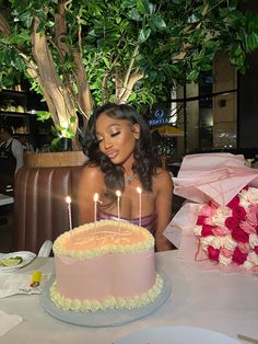 a woman sitting in front of a pink cake with lit candles on top of it