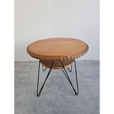 a wicker coffee table with black metal legs and a round wooden top on concrete flooring