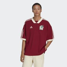 a man standing in front of a white background wearing a maroon shirt and beige pants