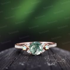 an engagement ring with a green and white stone in the center on top of a wooden surface