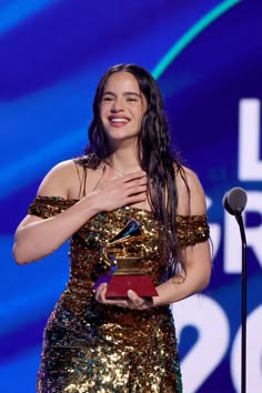 a woman standing in front of a microphone and holding an awards plaque with her right hand