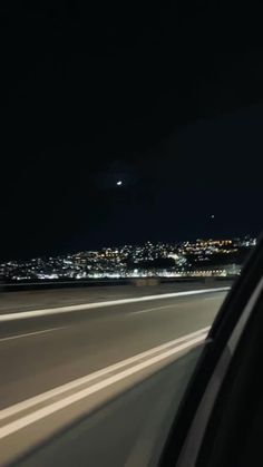 a car driving down a highway at night with the city lights in the back ground