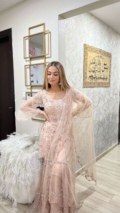 a woman standing in front of a white wall wearing a pink gown and shawl