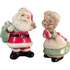 two ceramic figurines of santa and mrs claus, one holding a green bag