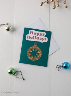 a green and gold christmas ornament sitting on top of a card next to ornaments