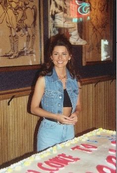 a woman standing in front of a cake with writing on it and smiling at the camera