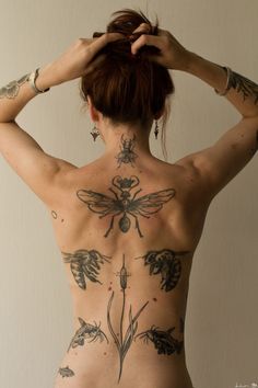 a woman with tattoos on her back is holding her hands to her head and looking down