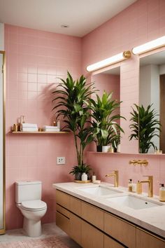 a bathroom with pink tiles and gold fixtures, including a plant in the mirror above the sink