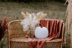 a white pumpkin sitting on top of a wicker chair next to dried grass and a red blanket