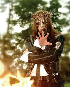 a man dressed in costume standing next to a fire pit with his hands outstretched out