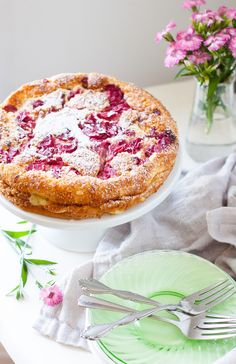 a pie sitting on top of a white table next to a green plate and pink flowers