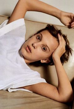 a young woman laying on top of a couch next to a white wall with her hand on her head