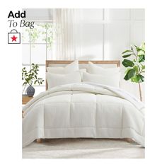 a bed with white comforter and pillows in front of a potted green plant